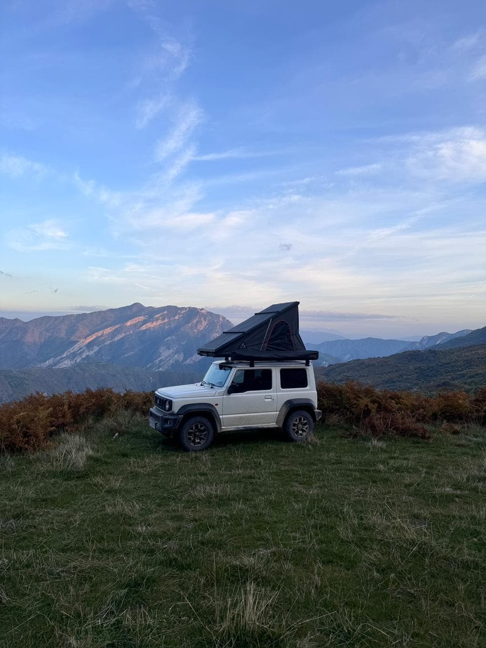 Jimny with rooftop tent open on an Albanian mountain ridge at dusk