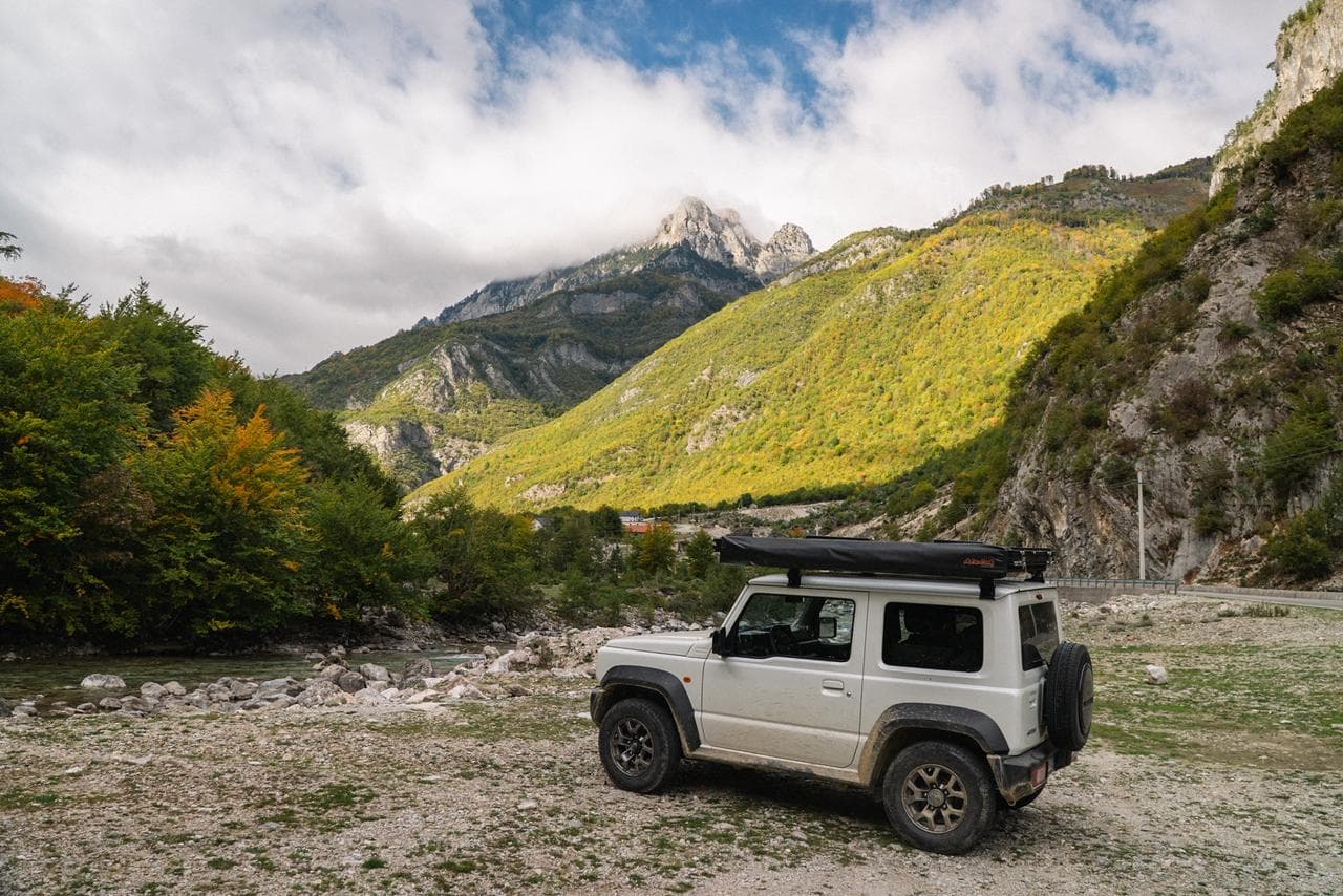 White Jimny parked in an Albanian river gorge with dramatic rocky peaks